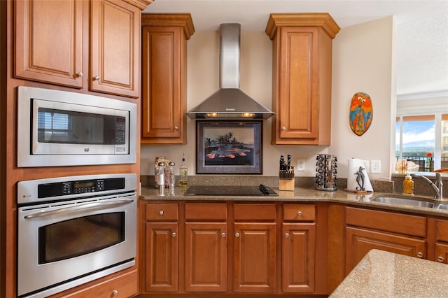 kitchen with stainless steel appliances, sink, dark stone countertops, and wall chimney range hood