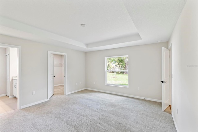 66 Ryland Dr, Palm Coast, FL 32164 - unfurnished bedroom with light carpet, a walk in closet, ensuite bath, a tray ceiling, and a closet