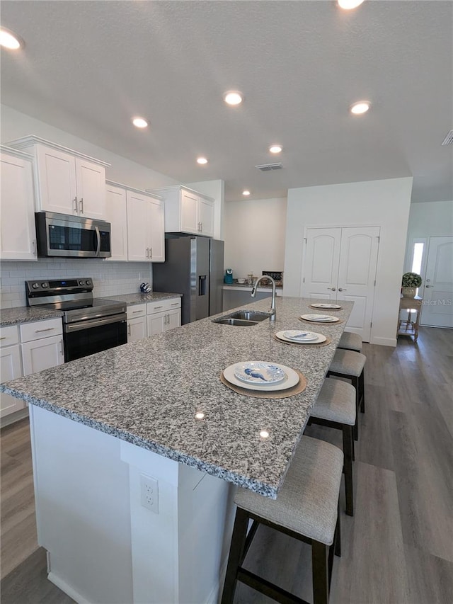 kitchen featuring stainless steel appliances, white cabinetry, a large island with sink, dark hardwood / wood-style flooring, and sink