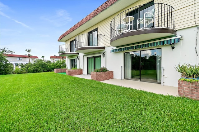 rear view of property featuring a balcony, a lawn, and a patio area