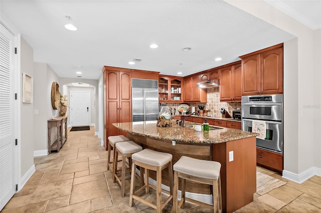 kitchen with an island with sink, stainless steel appliances, tasteful backsplash, light stone countertops, and sink