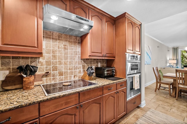 kitchen with double oven, extractor fan, black electric cooktop, and light stone countertops