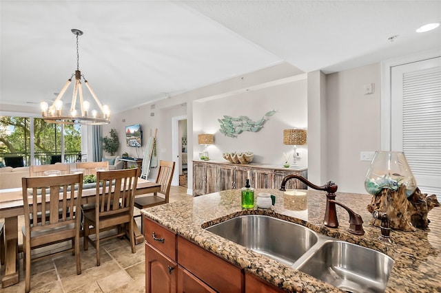 kitchen with light stone counters, sink, pendant lighting, and a chandelier