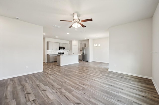 unfurnished living room featuring sink, light hardwood / wood-style floors, and ceiling fan with notable chandelier