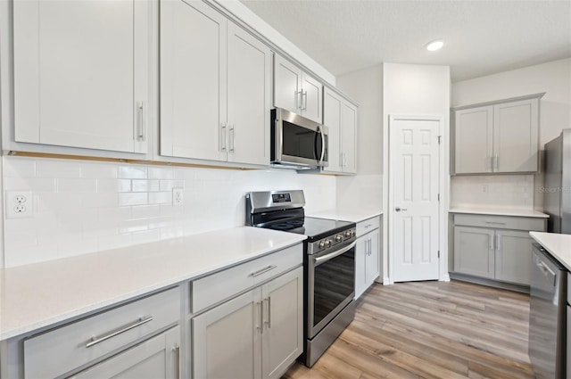 kitchen with light wood-type flooring, appliances with stainless steel finishes, gray cabinets, and decorative backsplash