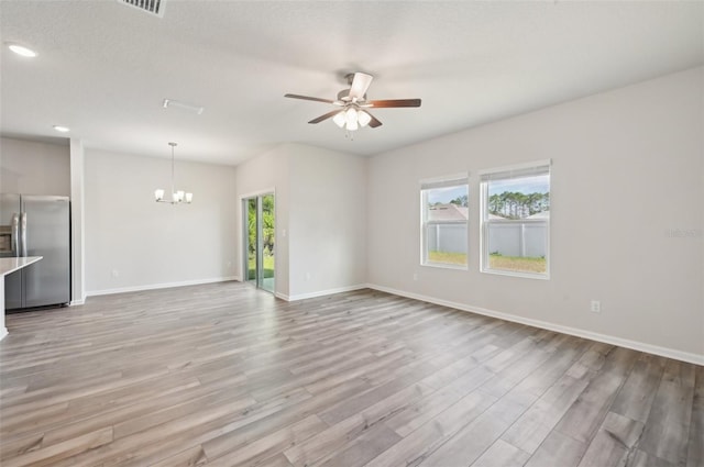 unfurnished living room featuring a textured ceiling, light hardwood / wood-style floors, a healthy amount of sunlight, and ceiling fan with notable chandelier