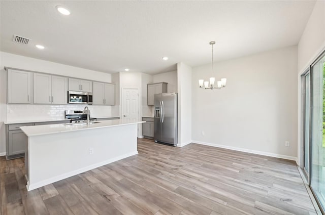 kitchen featuring appliances with stainless steel finishes, hanging light fixtures, decorative backsplash, light hardwood / wood-style floors, and sink