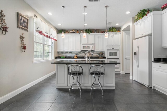 kitchen with a breakfast bar area, tasteful backsplash, white appliances, white cabinets, and dark tile patterned flooring