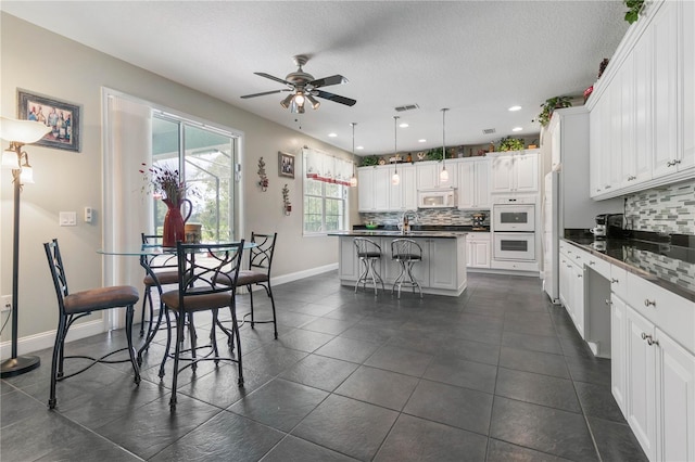 kitchen featuring white cabinetry, decorative backsplash, white appliances, a kitchen bar, and a kitchen island