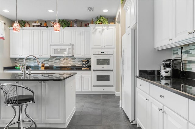 kitchen featuring tasteful backsplash, white appliances, hanging light fixtures, dark tile patterned flooring, and white cabinetry