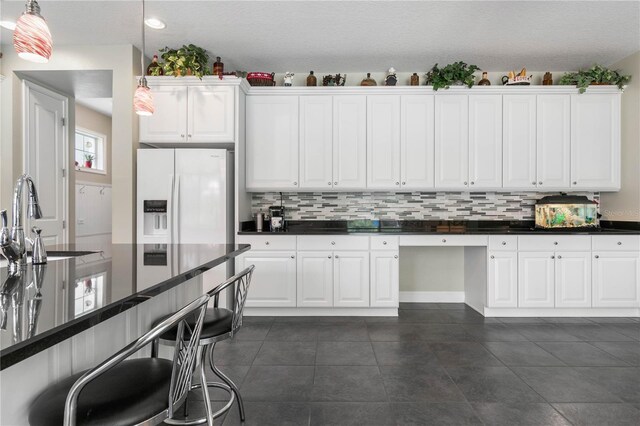 kitchen featuring white fridge with ice dispenser, tasteful backsplash, pendant lighting, and dark tile patterned flooring