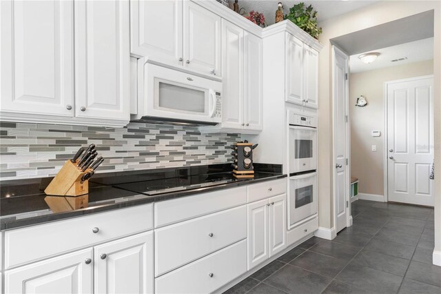 kitchen with white cabinets, dark tile patterned floors, tasteful backsplash, and white appliances