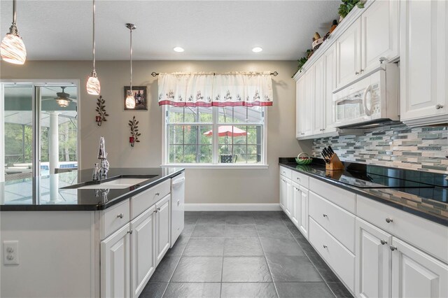 kitchen with white cabinetry, dark tile patterned floors, white appliances, sink, and backsplash