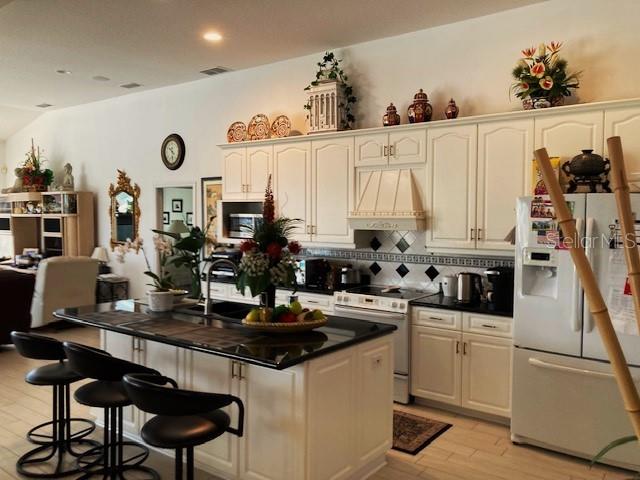 kitchen with tasteful backsplash, white appliances, light hardwood / wood-style floors, a center island, and custom range hood