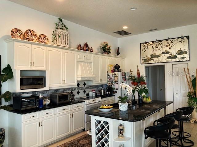 kitchen with white cabinetry, custom range hood, tasteful backsplash, a kitchen island, and appliances with stainless steel finishes