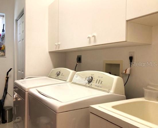 clothes washing area with sink, washing machine and dryer, and cabinets