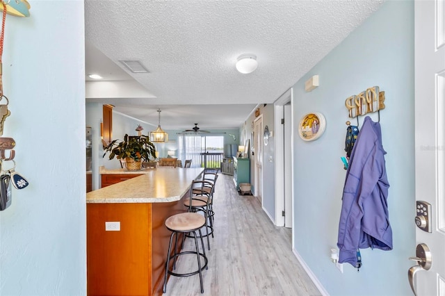 kitchen with ceiling fan, a breakfast bar area, light hardwood / wood-style flooring, and a textured ceiling