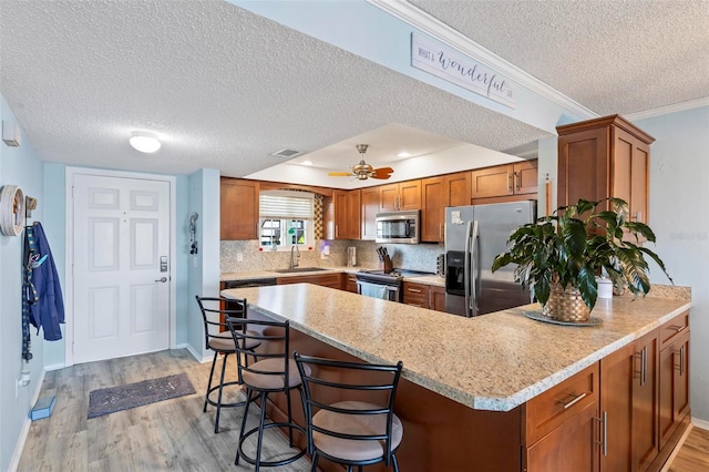 kitchen with ceiling fan, a kitchen bar, appliances with stainless steel finishes, light hardwood / wood-style flooring, and backsplash