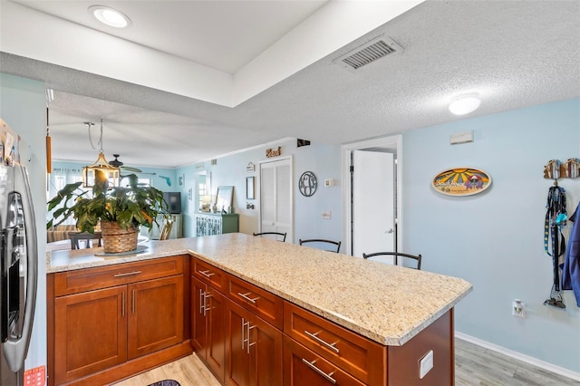 kitchen featuring light hardwood / wood-style floors, a textured ceiling, light stone counters, and kitchen peninsula