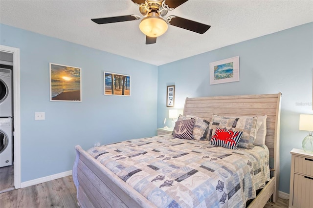 bedroom featuring ceiling fan, a textured ceiling, light wood-type flooring, and stacked washing maching and dryer