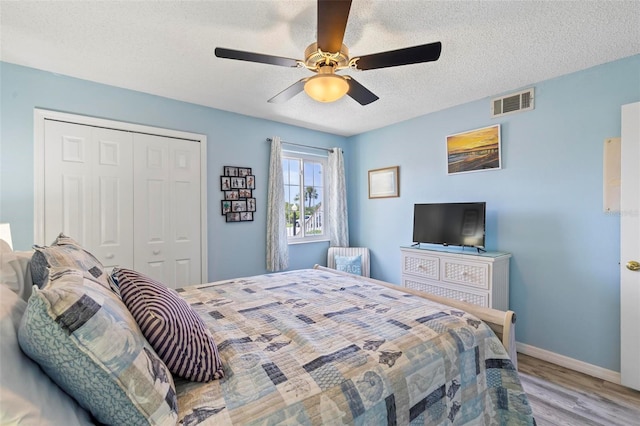 bedroom with light hardwood / wood-style floors, a textured ceiling, a closet, and ceiling fan