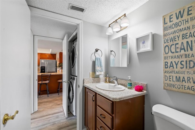 bathroom featuring vanity, wood-type flooring, stacked washer and clothes dryer, toilet, and a textured ceiling