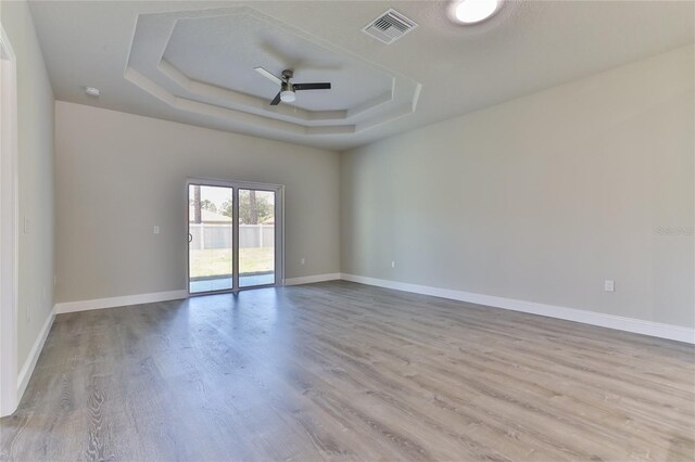 spare room with light hardwood / wood-style floors, a raised ceiling, and ceiling fan