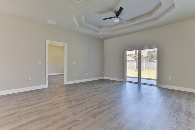 empty room featuring ceiling fan, light hardwood / wood-style floors, and a tray ceiling