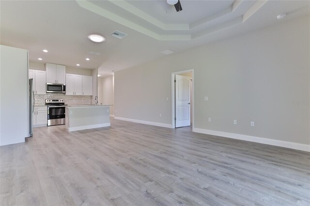 unfurnished living room featuring a raised ceiling, sink, ceiling fan, and light wood-type flooring