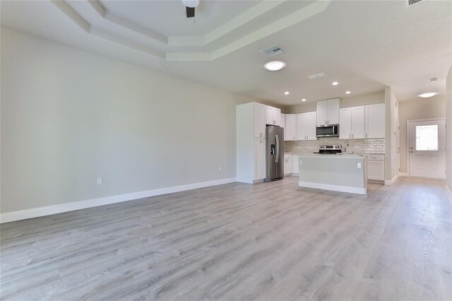 unfurnished living room featuring sink, a tray ceiling, ceiling fan, and light hardwood / wood-style flooring