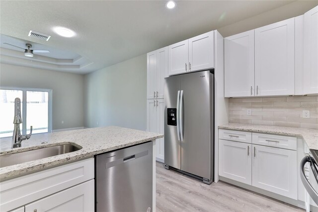 kitchen with stainless steel appliances, light wood-type flooring, light stone countertops, white cabinetry, and ceiling fan