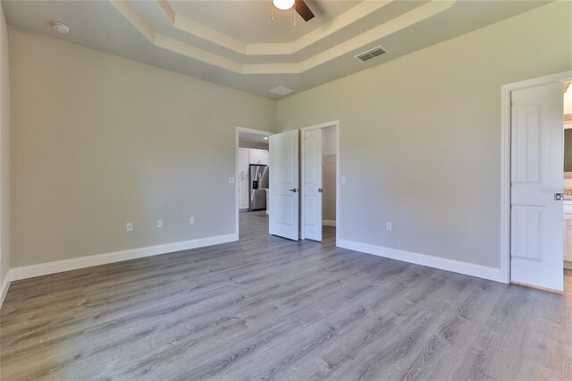 unfurnished bedroom featuring a raised ceiling, light hardwood / wood-style flooring, stainless steel refrigerator with ice dispenser, and ceiling fan