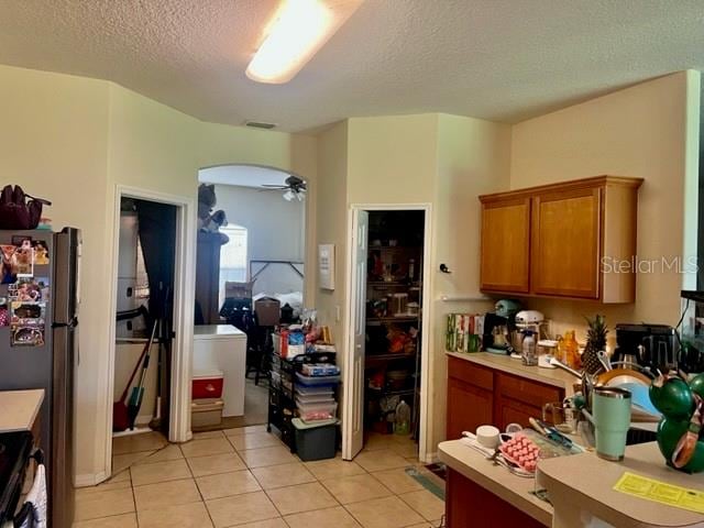 kitchen with light tile patterned flooring, stainless steel refrigerator, a textured ceiling, ceiling fan, and stove