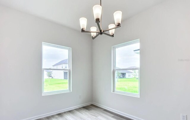 spare room featuring light wood-style floors, baseboards, and a notable chandelier