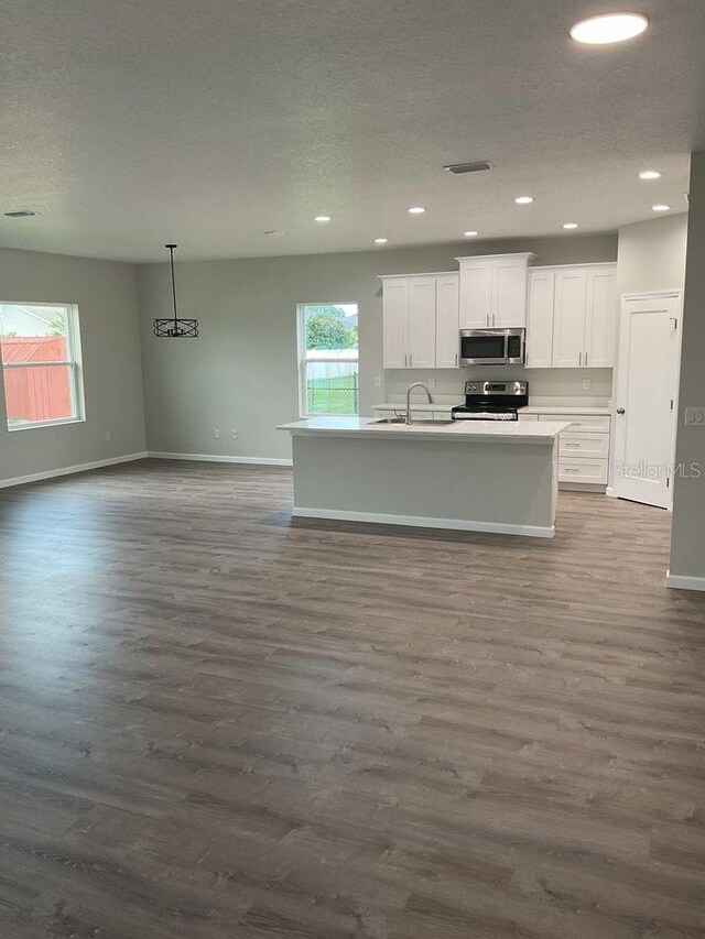 kitchen featuring a textured ceiling, stainless steel appliances, an island with sink, dark hardwood / wood-style floors, and white cabinets