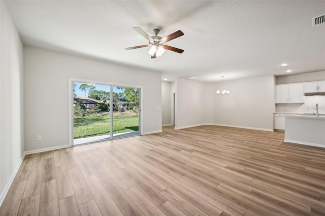 unfurnished living room featuring ceiling fan with notable chandelier, sink, a textured ceiling, and light wood-type flooring