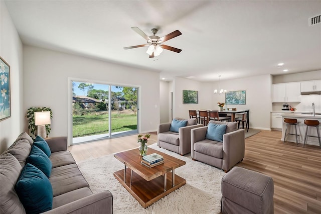 living room with sink, ceiling fan with notable chandelier, and light wood-type flooring