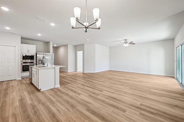 kitchen featuring ceiling fan with notable chandelier, stainless steel appliances, an island with sink, white cabinets, and decorative light fixtures