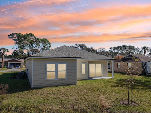 back house at dusk featuring central AC unit and a lawn