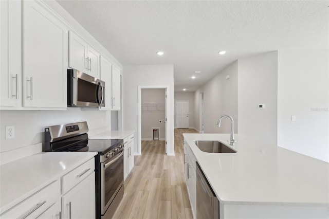 kitchen featuring sink, white cabinetry, a textured ceiling, light hardwood / wood-style floors, and stainless steel appliances