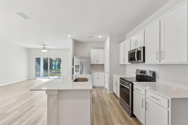 kitchen featuring appliances with stainless steel finishes, sink, light wood-type flooring, white cabinetry, and an island with sink