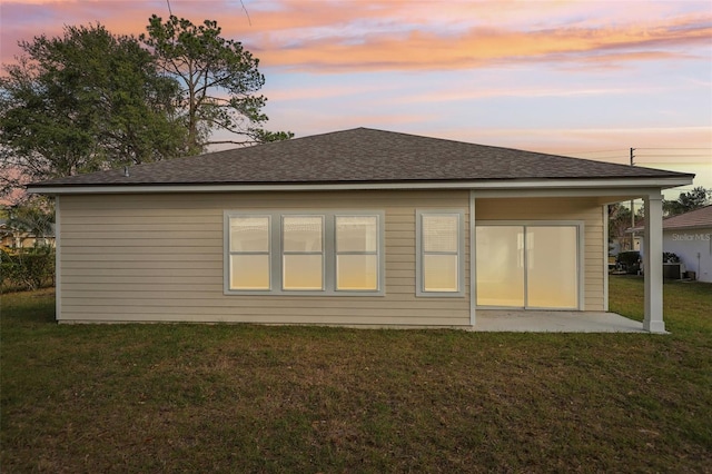 back house at dusk featuring a yard and a patio area