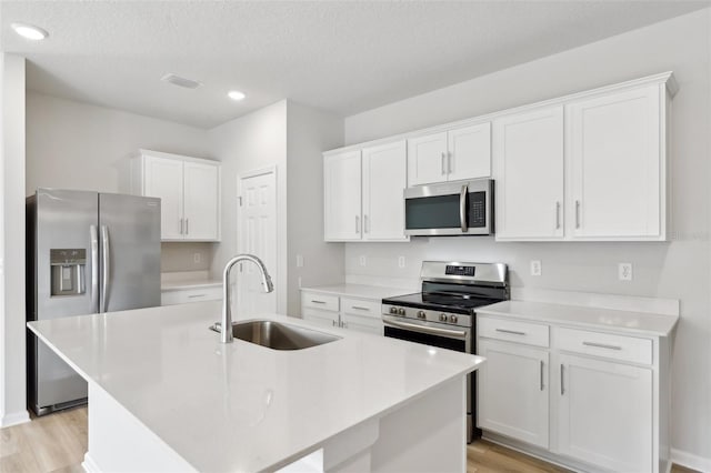 kitchen with appliances with stainless steel finishes, white cabinets, light hardwood / wood-style floors, sink, and a kitchen island with sink