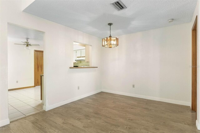 spare room featuring hardwood / wood-style flooring, ceiling fan with notable chandelier, and a textured ceiling