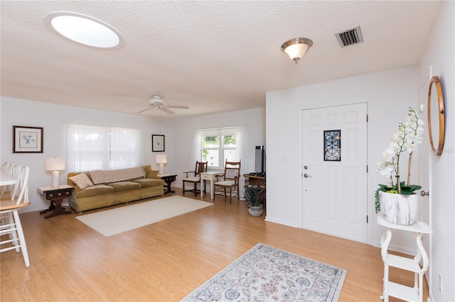 living room with a textured ceiling, light wood-type flooring, and ceiling fan