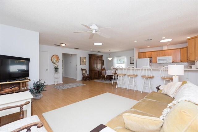 living room with light hardwood / wood-style floors, a textured ceiling, and ceiling fan