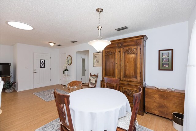 dining space with light wood-type flooring and a textured ceiling