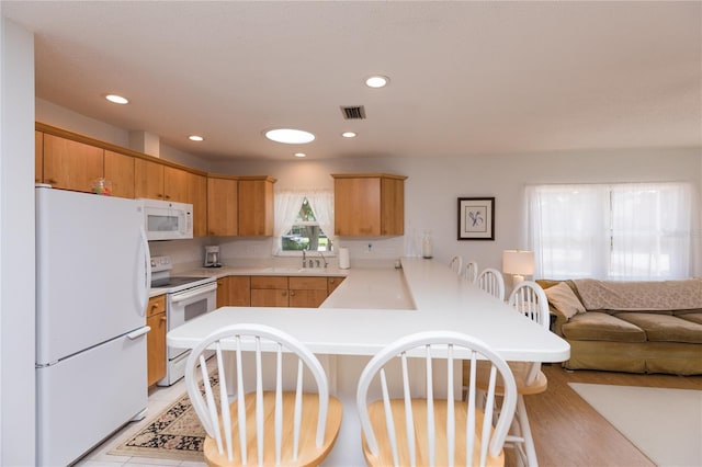 kitchen with white appliances, sink, light hardwood / wood-style floors, kitchen peninsula, and a breakfast bar