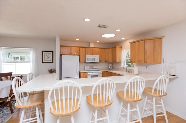 kitchen with light hardwood / wood-style flooring, white appliances, sink, kitchen peninsula, and a kitchen breakfast bar