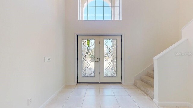 entrance foyer with tile patterned floors, stairway, french doors, baseboards, and a towering ceiling